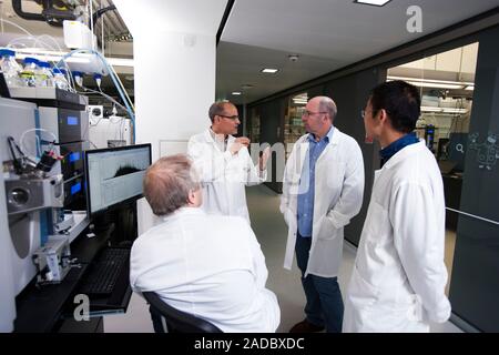 Proteomics and mass spectrometry service. Researchers talking in a laboratory that uses mass spectrometers to analyse proteins. This is part of a prot Stock Photo