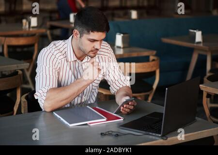 Having business chat. Adult man sits in cafe at daytime and using the laptop for the remote work Stock Photo
