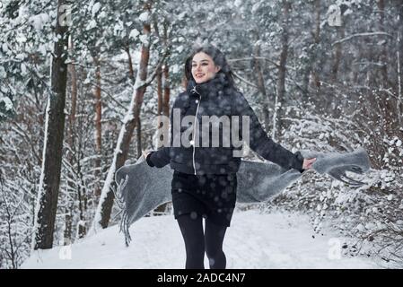 Running forward. Portrait of charming woman in the black jacket and grey scarf in the winter forest Stock Photo
