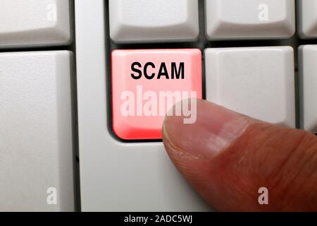 Online scam, conceptual image. Close-up of a finger pressing a button on a computer keyboard highlighted in red and labelled 'scam', representing onli Stock Photo