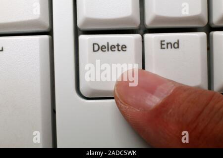 Digital deletion, conceptual image. Close-up of a finger pressing the delete button on a computer keyboard, representing the erasing of digital files Stock Photo