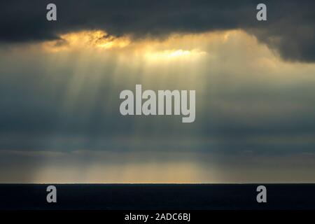 Sunlight streaming through small breaks in the clouds which act as a grid, allowing just small shafts of light to pass through to illuminate the horiz Stock Photo