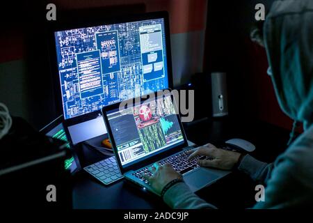 Computer hacking culture. Computer hacker typing on a laptop surrounded by other display screens. Photographed in Brussels, Belgium. Stock Photo