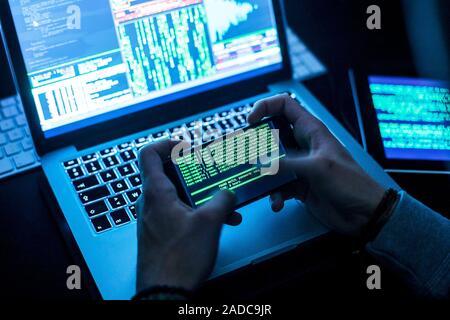 Hacker cracking a password. Computer hacker using a laptop and a handheld device that has been used to work out a password. Photographed in Brussels, Stock Photo