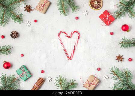 Christmas or Happy New Year composition. Frame made of fir tree branches, holiday decorations and gift boxes and heart on concrete background. flat la Stock Photo