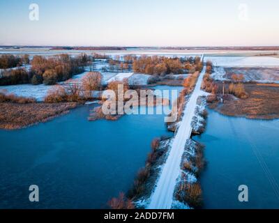 Aerial view of lake and snow covered bridge over it during nice sunrise in Lithuania - Winter landscape Stock Photo