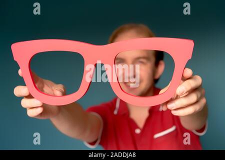 Cheerful man in a red shirt holding big red glasses and looking through Stock Photo