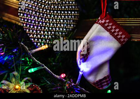 Christmas hanging decorations on fir tree. Decorated Christmas tree. Fir branch with Christmas stocking surrounded by lights and garlands. Stock Photo