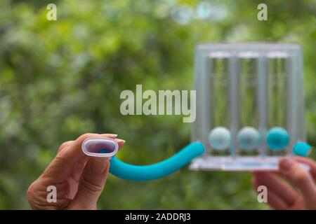 Hand holding a turquoise Spirometer deep breathing incentive flow exercise device. Healthcare cardiac surgery recovery and lung function therapy with Stock Photo