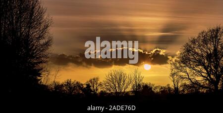 Sun and crepuscular rays shining through clouds in winter on a late afternoon near sunset. The beams are named for the Latin for twilight, the time of Stock Photo