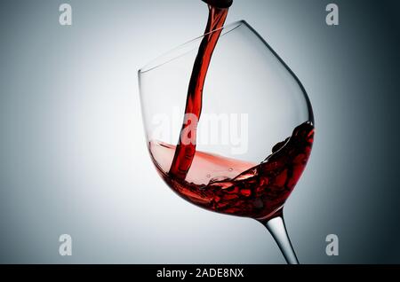 Pouring red wine into tilted glass, plain background. Stock Photo