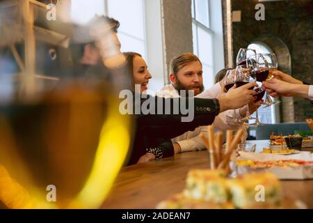 Happy co-workers celebrating while company party, corporate event. Young caucasian people in business attire talking, drinking wine. Concept of office culture, teamwork, friendship, holidays, weekend. Stock Photo