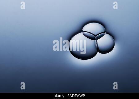 Three air bubbles overlapping on smooth dark liquid surface. Stock Photo