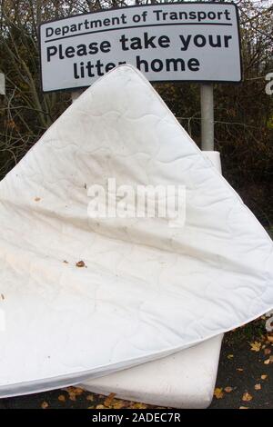 Flytipped domestic bedding. Two double bed mattresses illegally discarded as waste in a layby against a 'please take your litter home' sign. Photograp Stock Photo