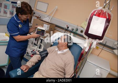 Day Care Manager taking blood pressure whilst Haematology day patient is having a blood transfusion. Stock Photo