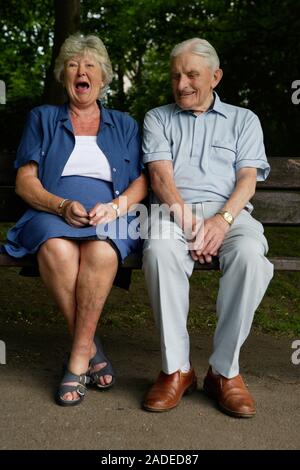 Older couple sharing a joke whilst sitting on a bench in the park . Stock Photo