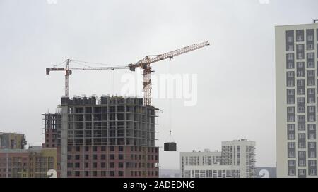 A construction crane lifts a load. Tower Crane on a Construction Site Lifts a Load at High-rise Building. The process of building a multi-story modern Stock Photo