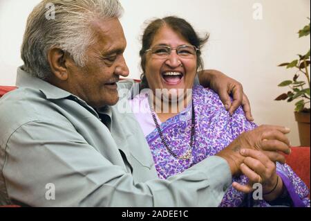 Older couple sitting on the sofa at home, smiling. Stock Photo