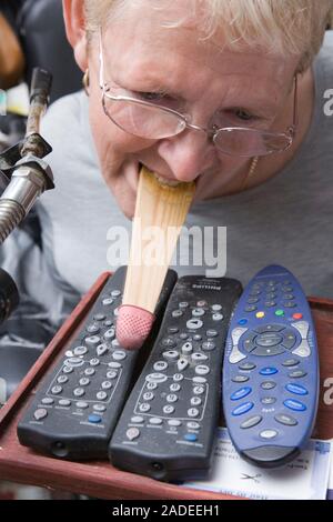 Woman with cerebral palsy using her mouth to operate a TV remote control. Stock Photo