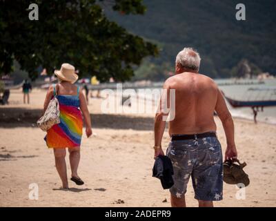 Old couple walking swimsuit in sandy beach coast line whaite sands