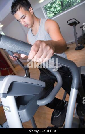 Young man using the crosstrainer at gym. Stock Photo