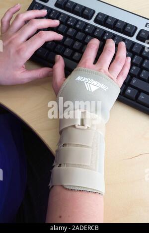 Office worker typing on a computer whilst wearing an elasticated wrist support to help alleviate repetitive strain injury (RSI), RSI most commonly aff Stock Photo