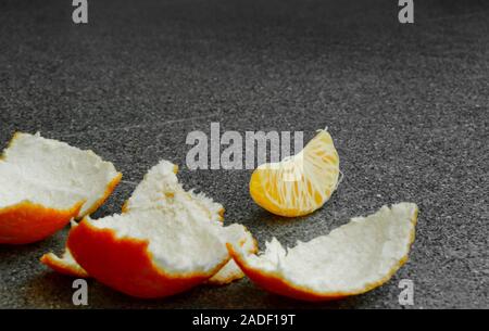 An orange light tangerine on a table, the paring is peeled and one slice lays on the table Stock Photo