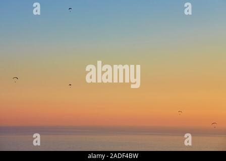 Silhouette of powered paraglider soaring flight over the sea against marvellous orange sunset sky. Paragliding - recreational and competitive adventur Stock Photo