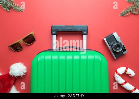 Christmas holiday minimal creative composition made of suitcase, sunglasses,Santa hat, candy cane, retro photo camera and fir branches on red backgrou Stock Photo