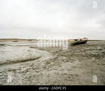 Low tide. Fishing boats and a water channel at low tide. This large area of mud flats is exposed twice daily by the sea as it recedes during the ebb t Stock Photo