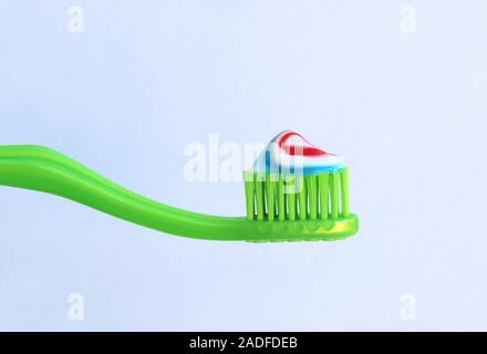 close-up of a green toothbrush with striped toothpaste in front of a gray background with copy space Stock Photo