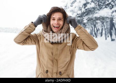 Handsome Man Pulling Scarf On Head Standing In Snowy Forest Stock Photo