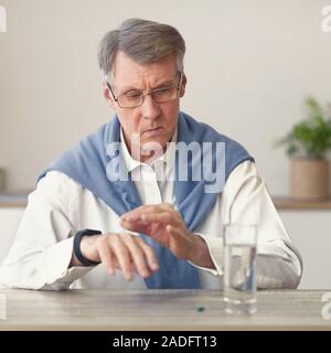 Elderly Man Looking At Smartwatch Sitting Taking Medicines At Home Stock Photo