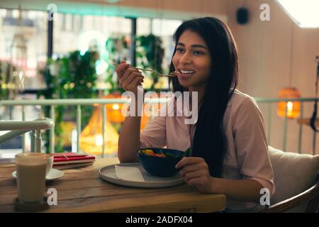 Long haired woman thoughtfully eating salad it the cafe Stock Photo
