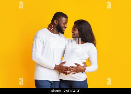 Cheerful afro pregnant couple having conversation over yellow background Stock Photo