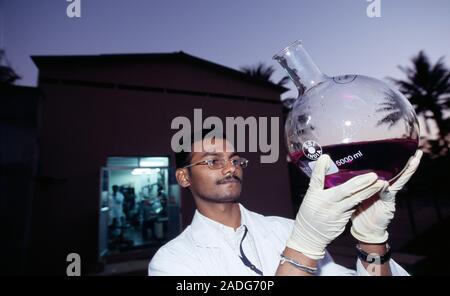 Bioscientist checking the clarity of a sample of liquid in a round-bottomed flask. Photographed at Biocon, a biotechnology company in Bangalore, India Stock Photo