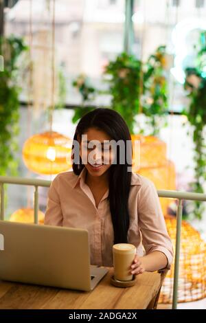 Long haired smiling woman with tasty latte and laptop Stock Photo