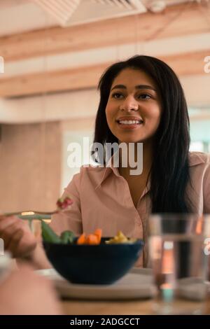 Dark haired happy woman eating her meal and smiling Stock Photo