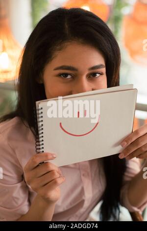 Dark haired woman hiding behind the drawn smile Stock Photo