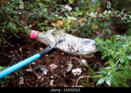 closeup of someone, in a forest, collecting a used plastic bottle with a grabber arm, as an action to clean the natural environment Stock Photo