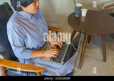 Asian businesswoman sitting at armchair and using laptop  Stock Photo