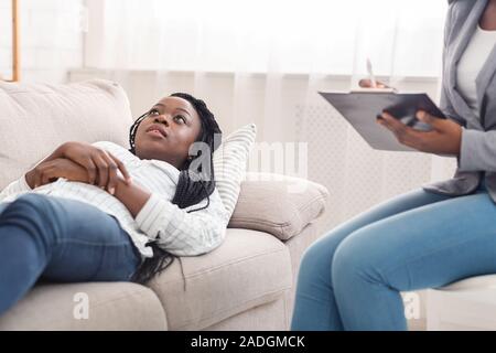 Depressed young black woman lying on couch during psychotherapy session Stock Photo