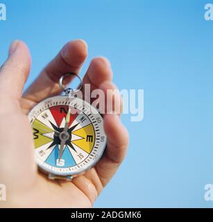 Magnetic compass. Hand holding a compass against a blue sky. The compass has a free-swinging magnetised needle, which is seen pointing to North on the Stock Photo