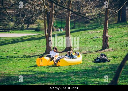 couple laying on yellow inflatable mattress in city park. reading book. drinking smoothies Stock Photo