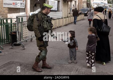 Hebron, West Bank. 4th December, 2019. A young Palestinian girl reaches out to an IDF soldier on patrol in Hebron. Israeli Defense Minister Bennett recently announced his approval of the establishment of a new Jewish neighborhood in the predominantly Palestinian city of Hebron near the old fruit and vegetable market. The land, purchased by Jews living there in the early 19th century, was abandoned after the 1929 massacre in which 67 Jews were murdered by Arab rioters. Credit: Nir Alon/Alamy Live News. Stock Photo