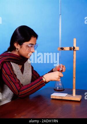 Chemistry experiment. Student performing an iodometric titration. A measured volume of a solution from a burette (down centre right) is dripped into a Stock Photo