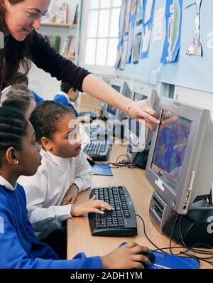 Schoolchildren using computers at school. The class teacher is pointing to something on a computer screen. Stock Photo