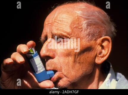 Asthma relief. Elderly man using an aerosol inhaler to control an asthma attack. Asthma attacks vary in severity from breathlessness, dry cough, wheez Stock Photo