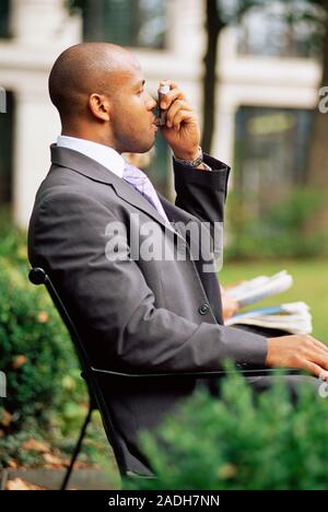 MODEL RELEASED. Using asthma inhaler. Man using his inhaler to treat an asthma attack. Asthma is a condition in which the small airways (bronchioles) Stock Photo