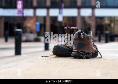 A portrait layout of a pair of old worn out work boots shoes sitting on a concrete wall. Stock Photo